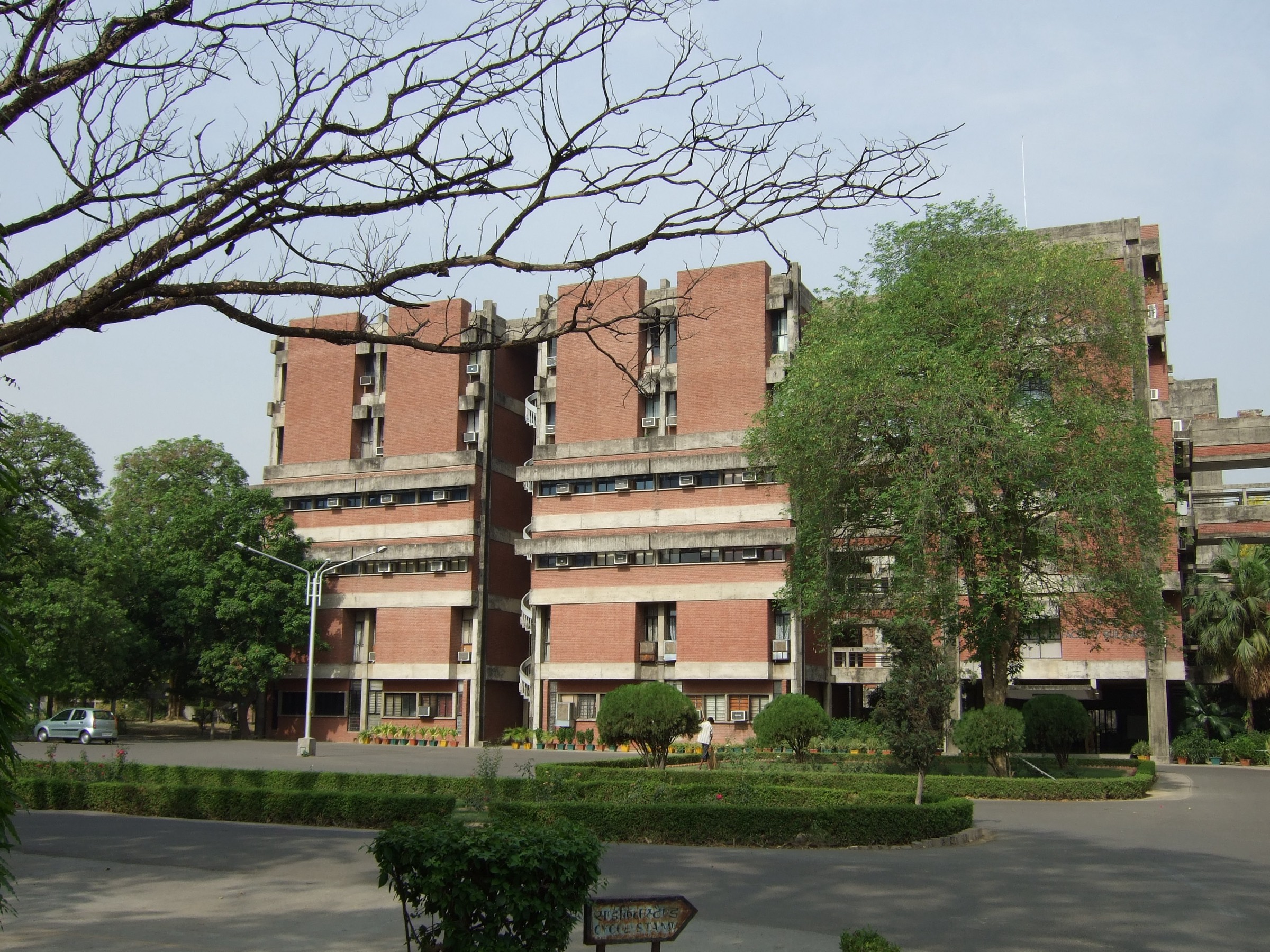 The red-brick Faculty Building at IIT Kanpur seen across a garden, framed by a bare tree