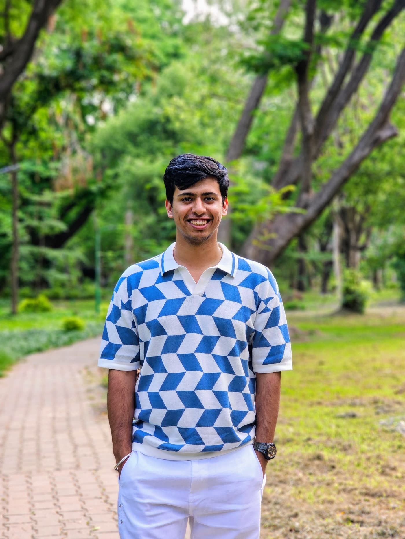 Aryan in a blue and white patterned shirt on a path through green trees