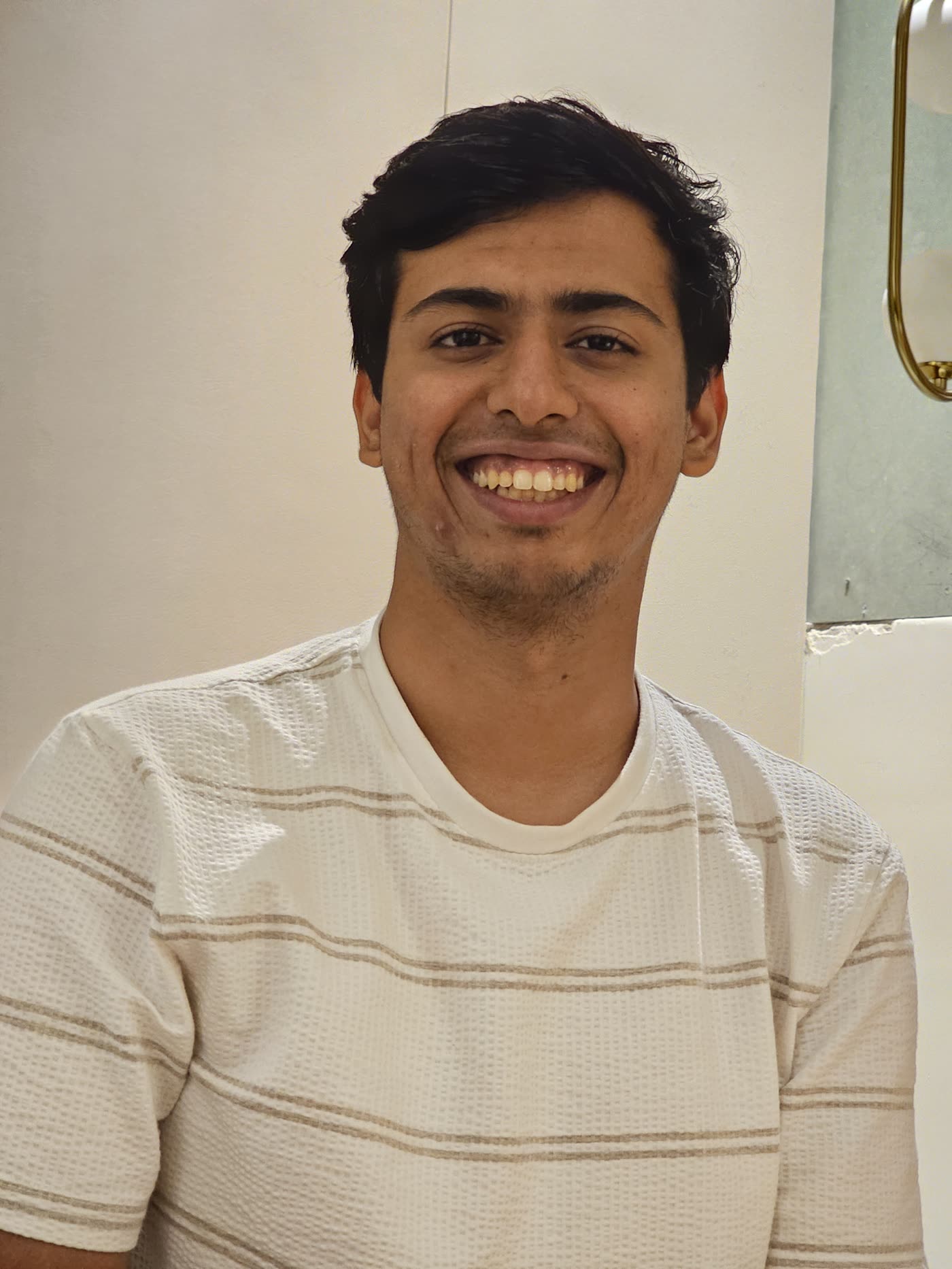Aryan Kalra smiling at the camera in a white striped T-shirt